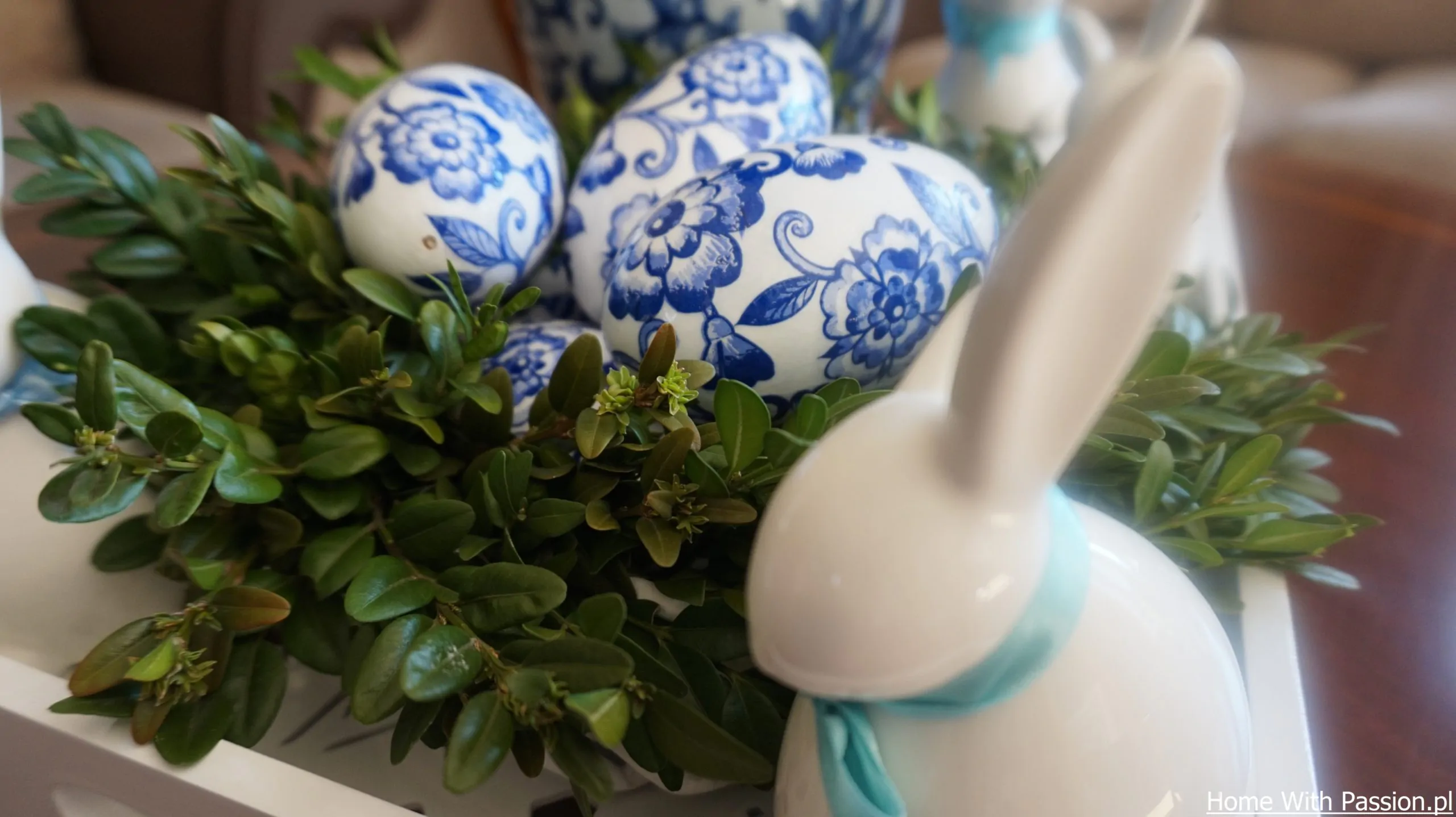 Dekoracja wielkanocna DIY w stylu hampton – jajko w niebieski wzór wśród zielonych gałązek i ceramiczny królik