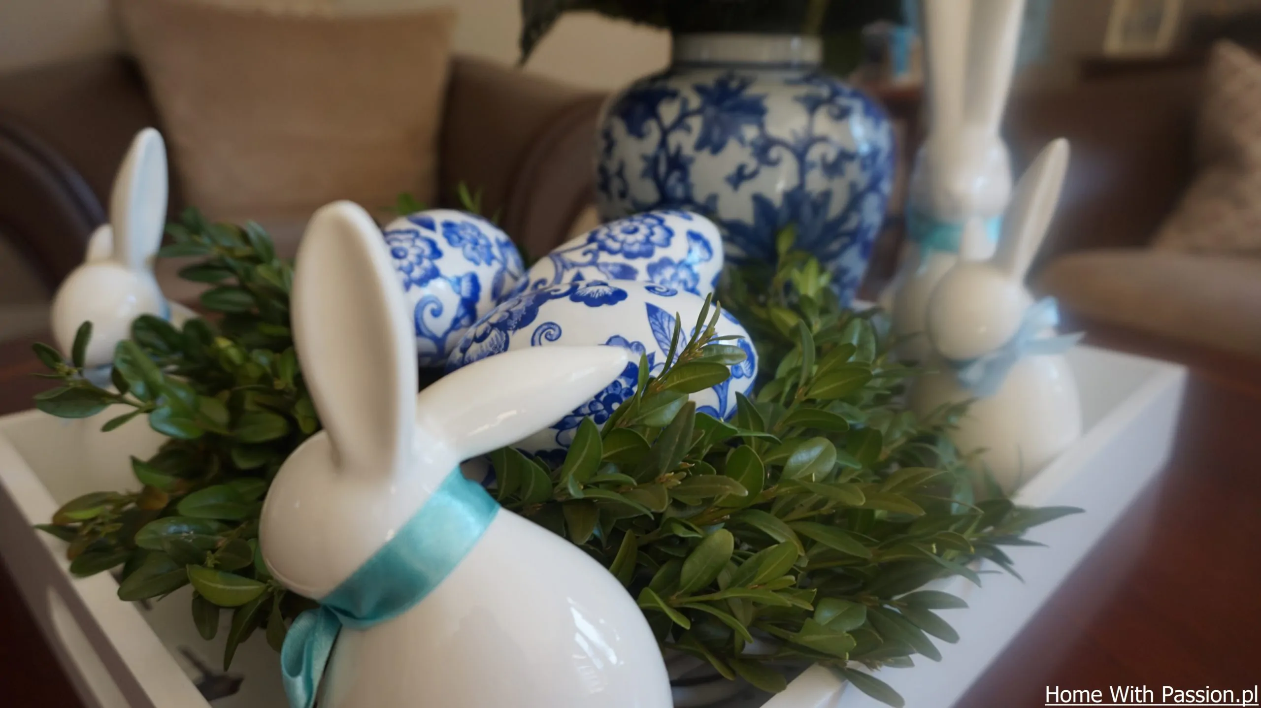 Kompozycja wielkanocna w stylu hampton – dekoracyjne jajka z niebieskim wzorem wśród zieleni i ceramicznych królików