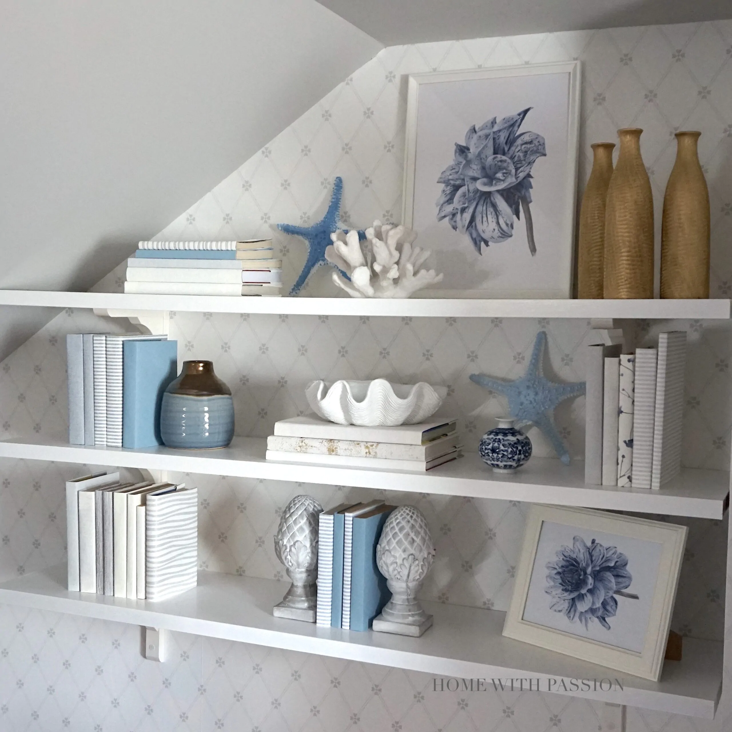 Stylowe białe półki ścienne z dekoracjami w odcieniach błękitu i złota, książki, wazony i koralowce – elegancka aranżacja półek w salonie w stylu hampton