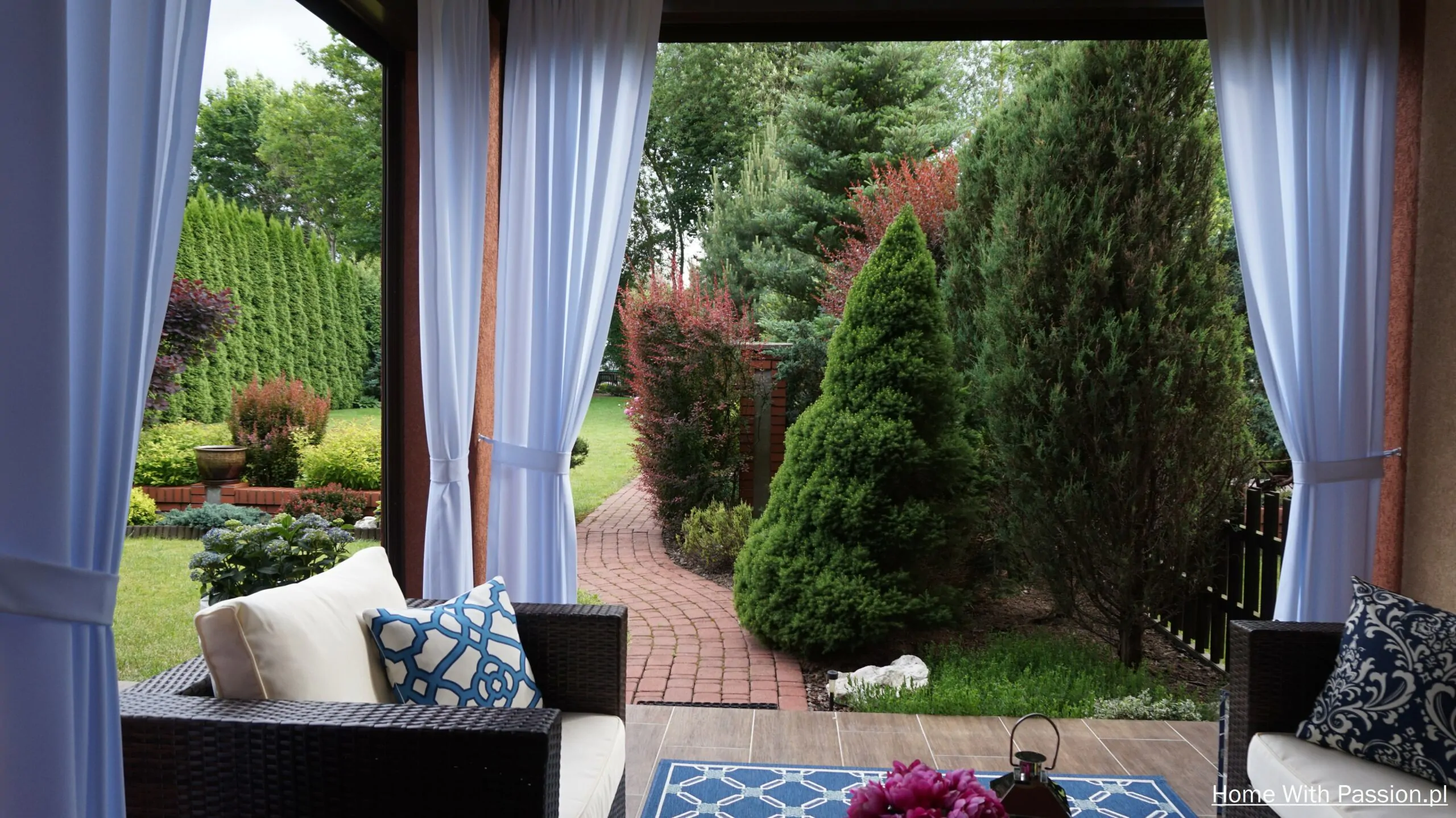 Widok z tarasu w stylu Hampton na zadbany ogród z zielenią i ścieżką ogrodową